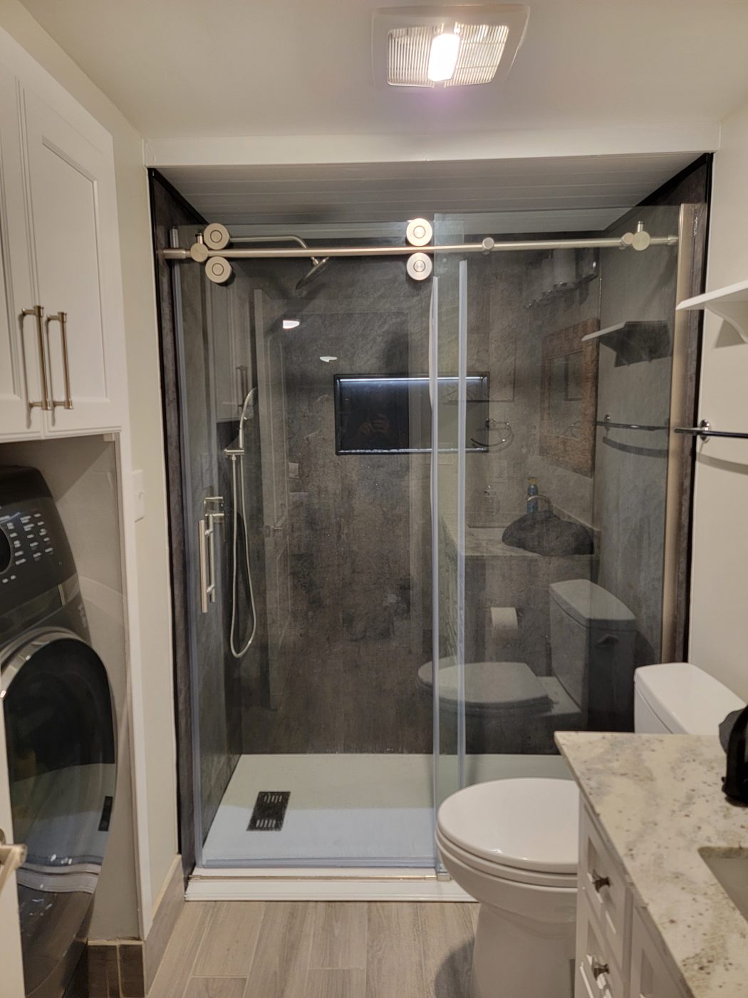 A walk-in shower with a charcoal accent and a lit niche, converted from an old tub